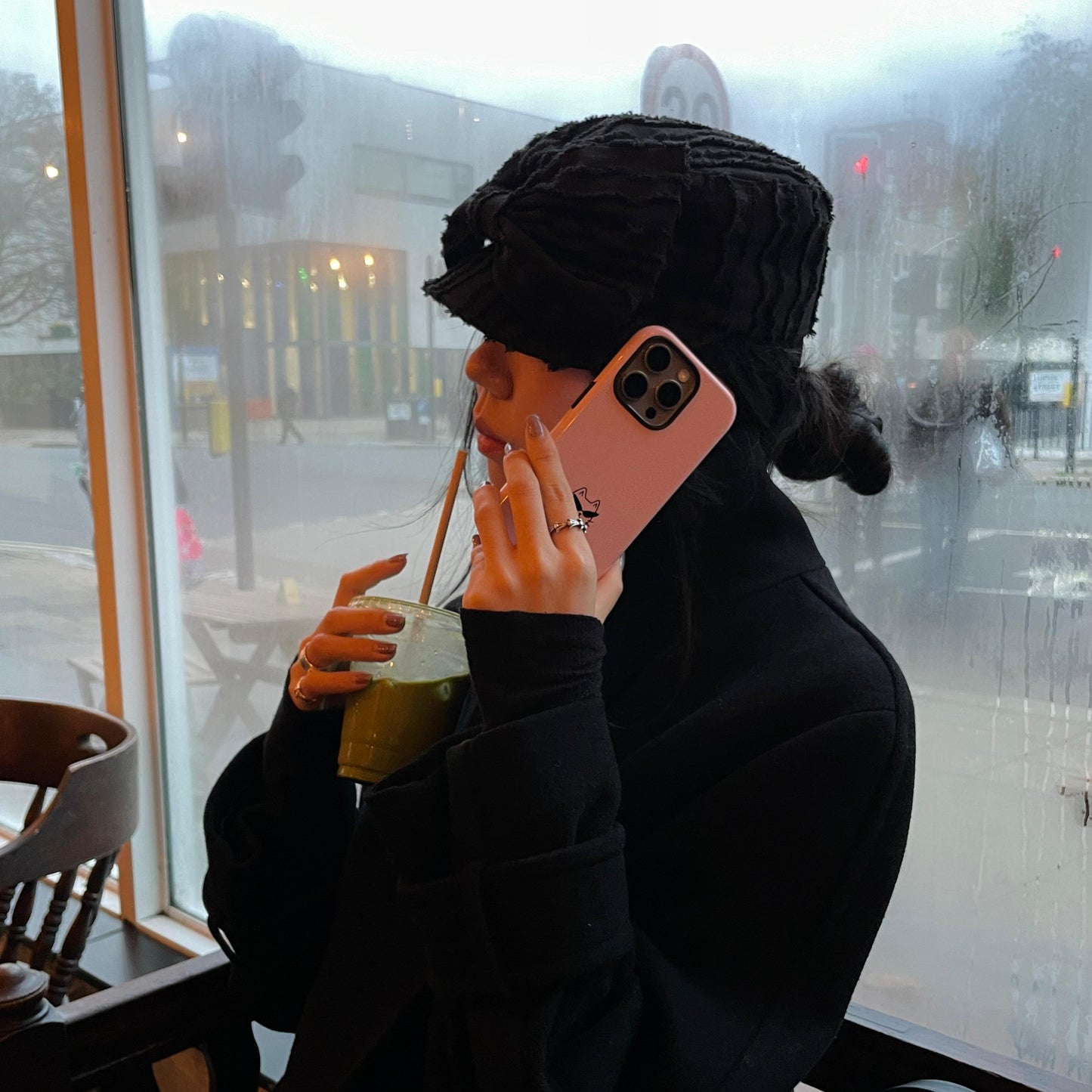 Person sitting in a cafe, using a phone with a pink case, holding a drink.