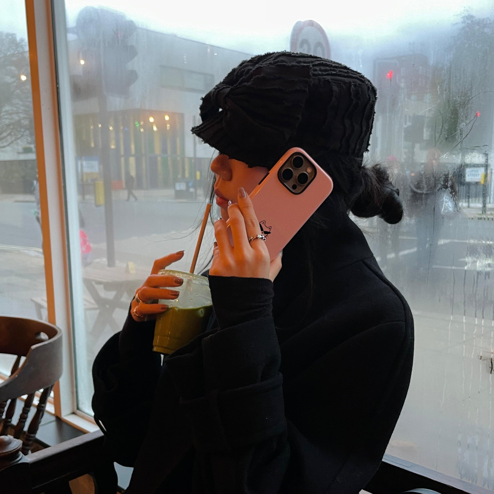 Person sitting in a cafe, using a phone with a pink case, holding a drink.