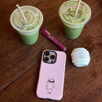 Pink phone case with a cartoon design on a wooden surface with green drinks and a lip balm.